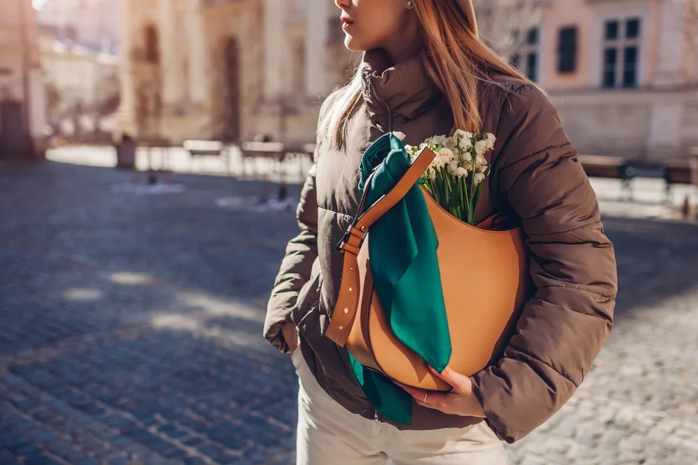 Medium shot of a woman holding a leather handbag with a bouquet of flowers and a tied scarf