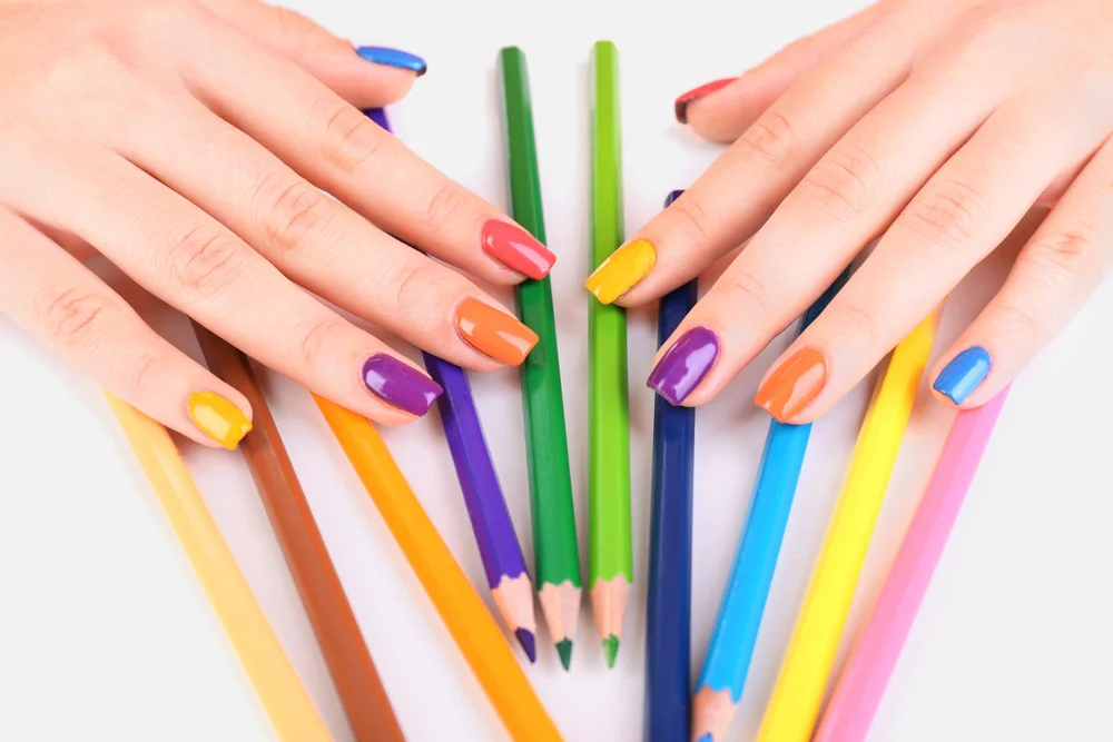 Multicolor female manicure and colored pencils isolated on a light grey surface
