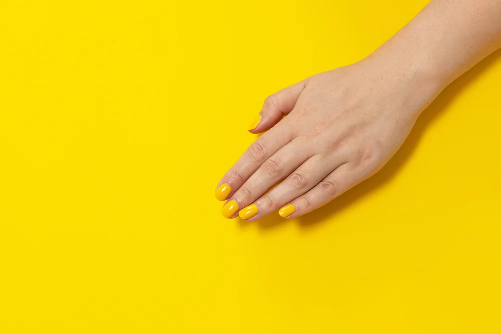 Hand with a yellow manicure in a yellow background