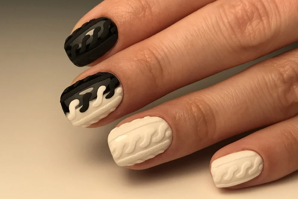 Close-up of black and white manicure with several sweater-like 3D patterns