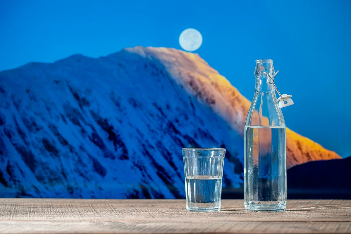 Bottle of pure water and a glass on a wooden table with the snowy background of the Himalayan mountains and full moon, nearby