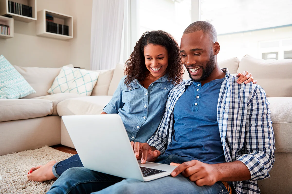 Young black couple using a laptop sitting on the floor at home