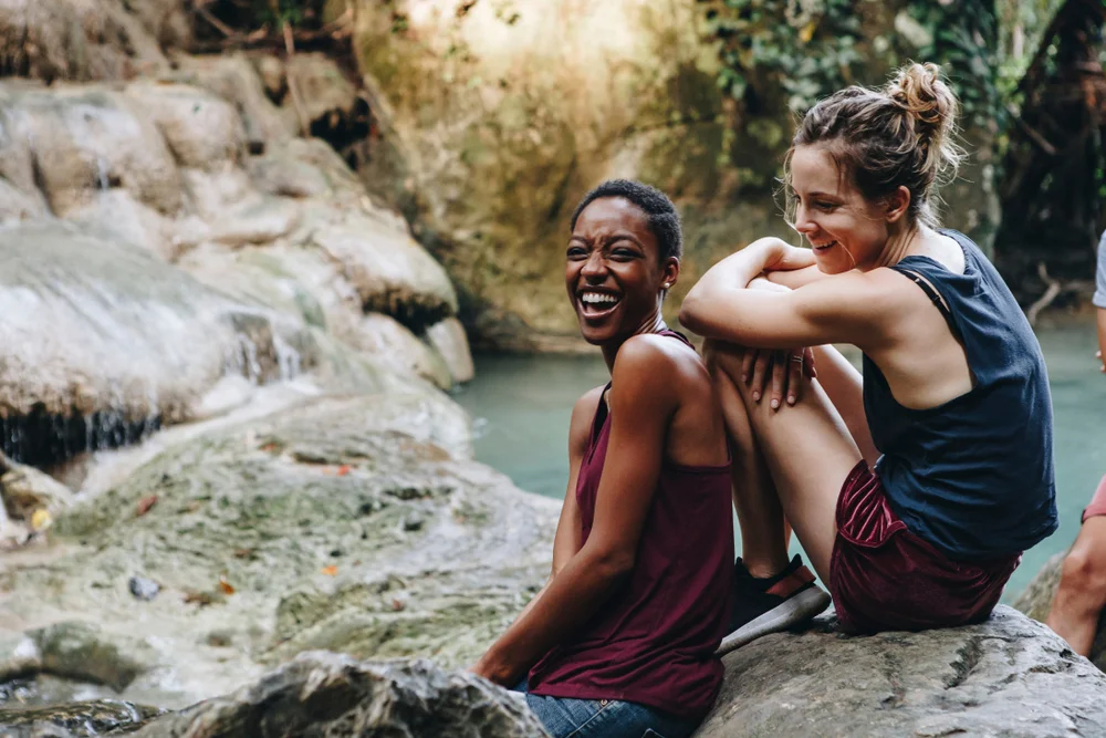 Two girlfriends hanging out and laughing by a waterfall