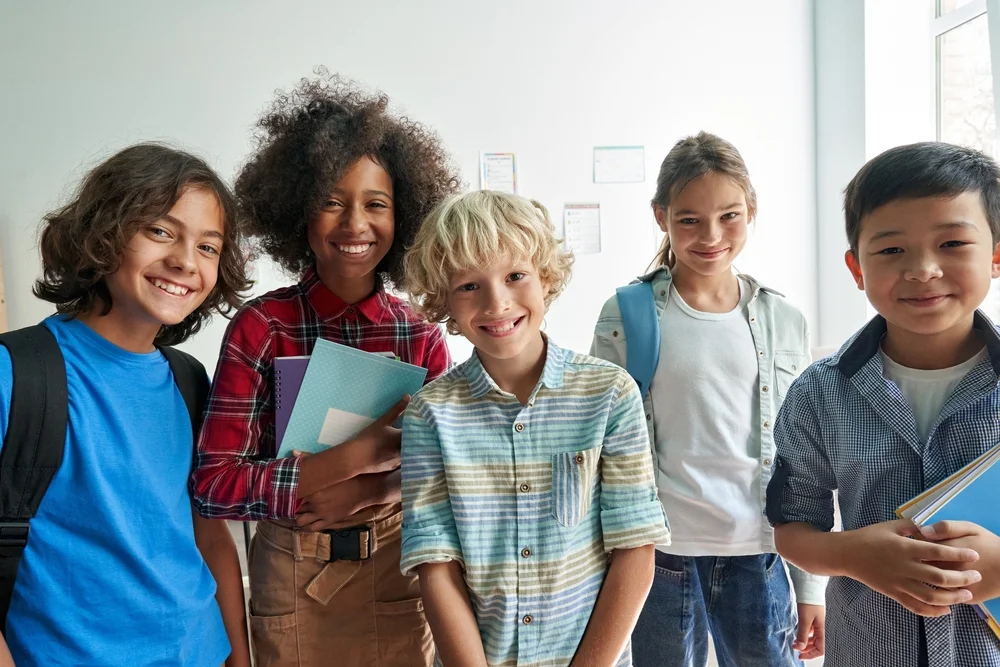 Group of happy, diverse, junior school students looking at camera in a classroom