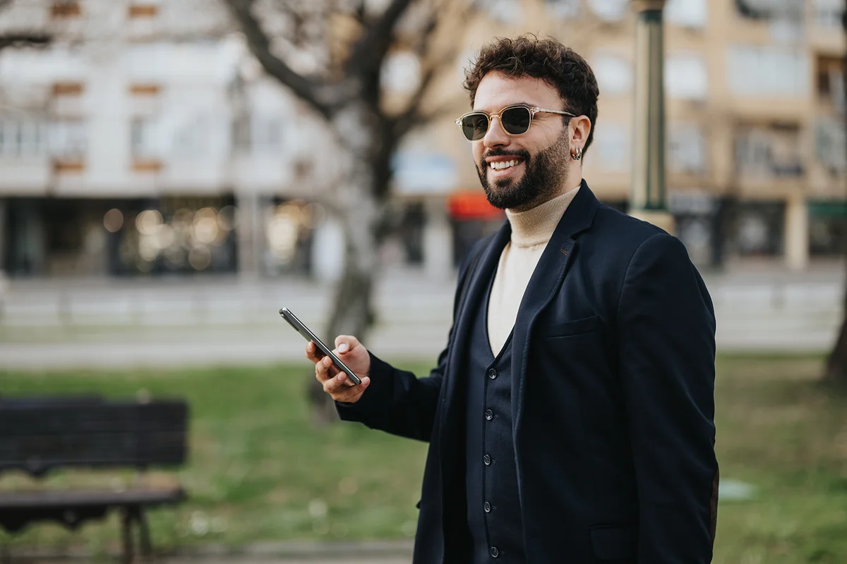 A well-dressed man stands in a city park engrossed in his mobile phone