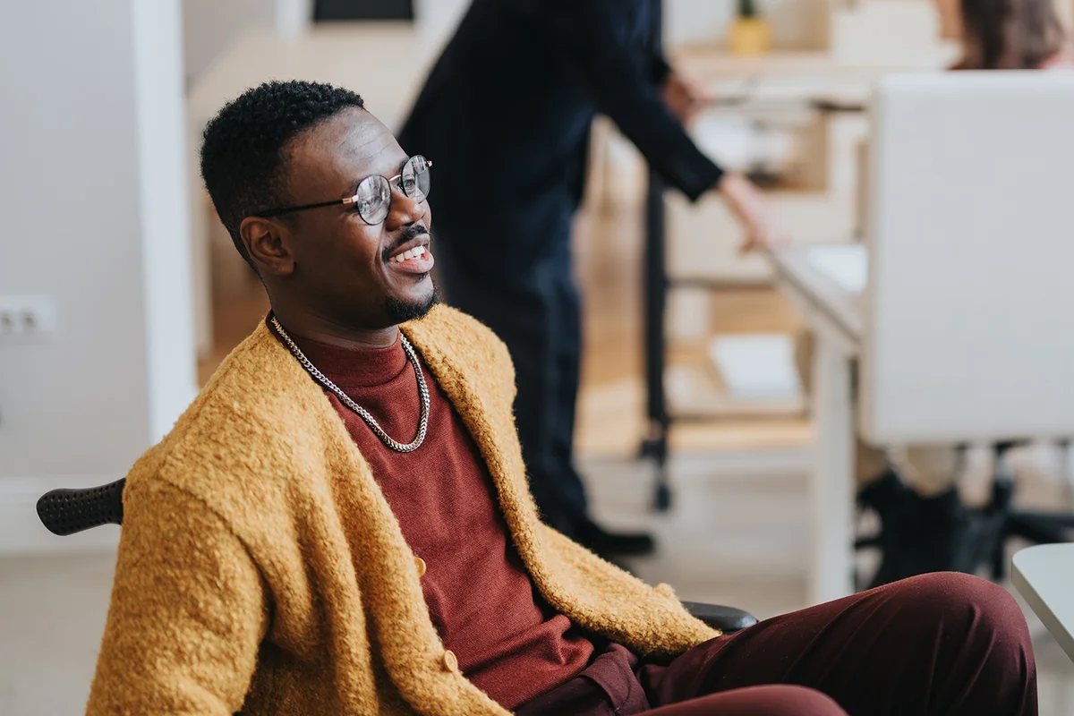 A cheerful man in a yellow cardigan has a relaxed conversation in a modern office