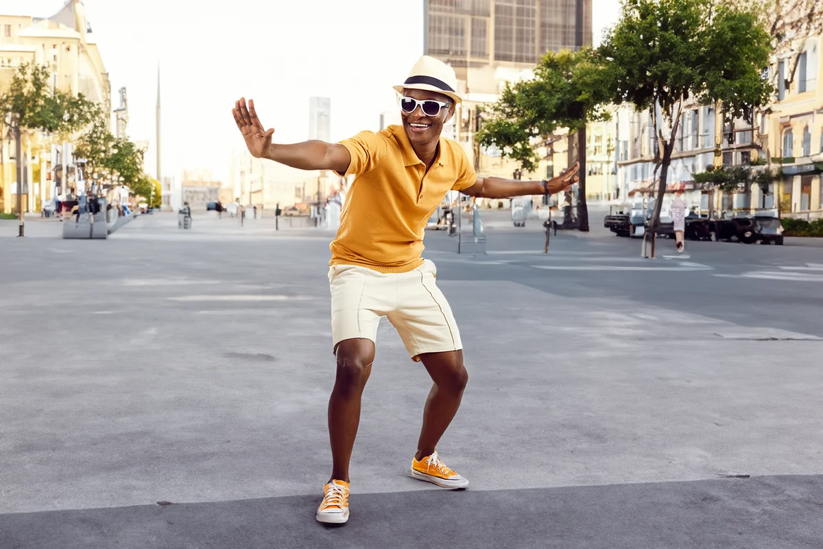 Cheerful stylish african american man having fun dancing on light beige background.