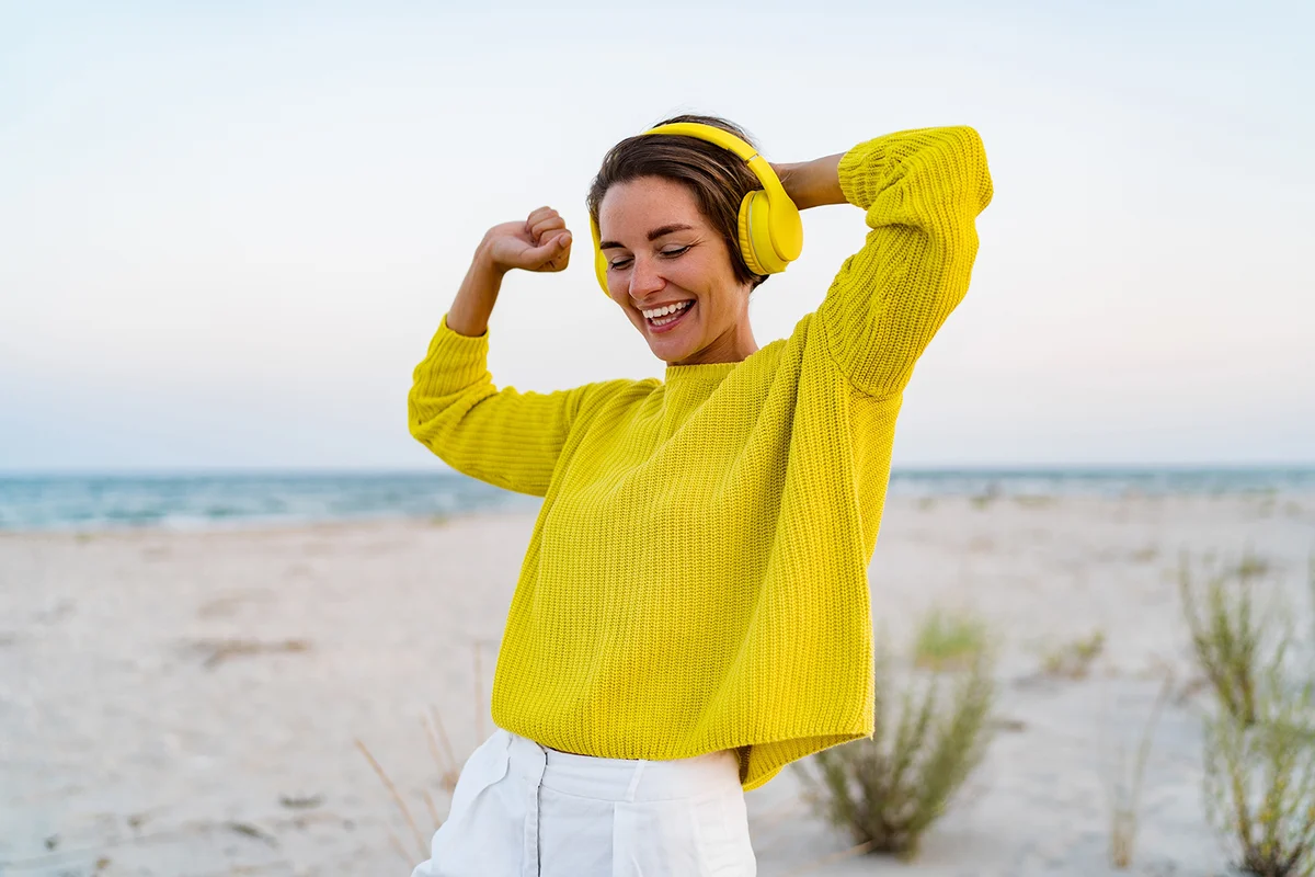 attractive happy smiling woman listening to music in colorful yellow headphones on beach