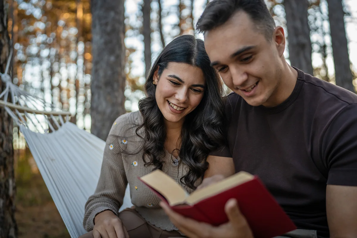 Man and woman young adult couple in nature hold and read book in love