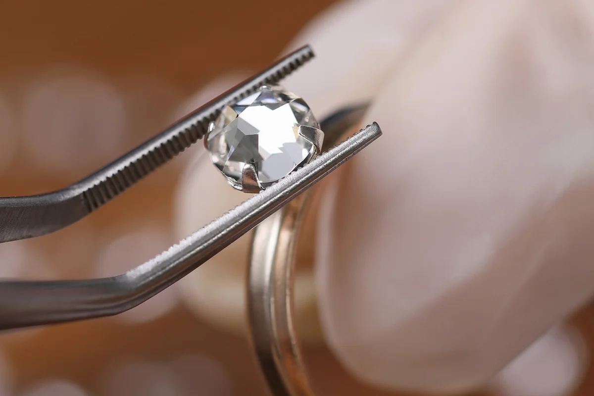 Jeweler install loose cut moissanite color round brilliant in ring DIY material diamond against wood table background.