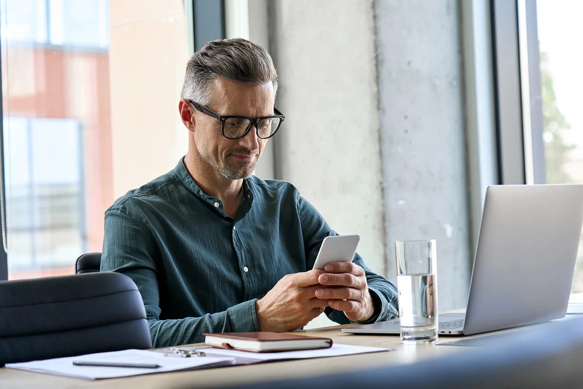 Smiling mature businessman holding smartphone sitting in office