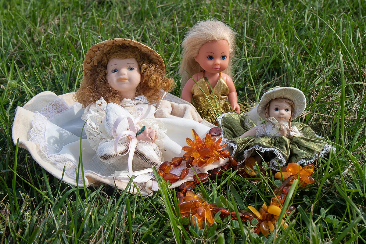 Three beautiful ceramic old dolls with orange amber beads on the grass.