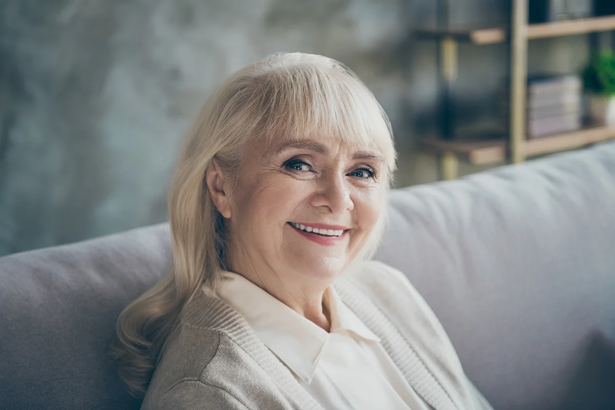 Closeup photo of amazing adorable aged granny homey good mood toothy beaming smiling sitting comfort sofa divan living room indoors