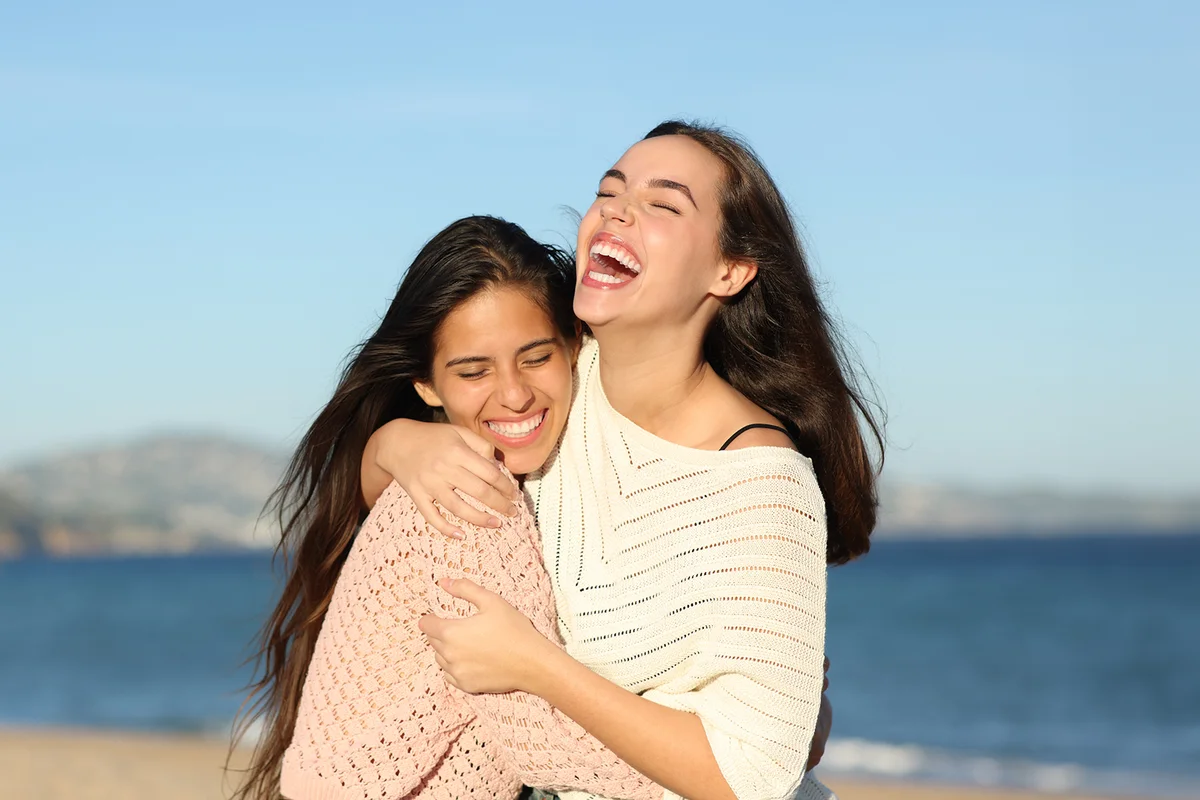 Happy friends meeting and hugging laughing very funny on the beach
