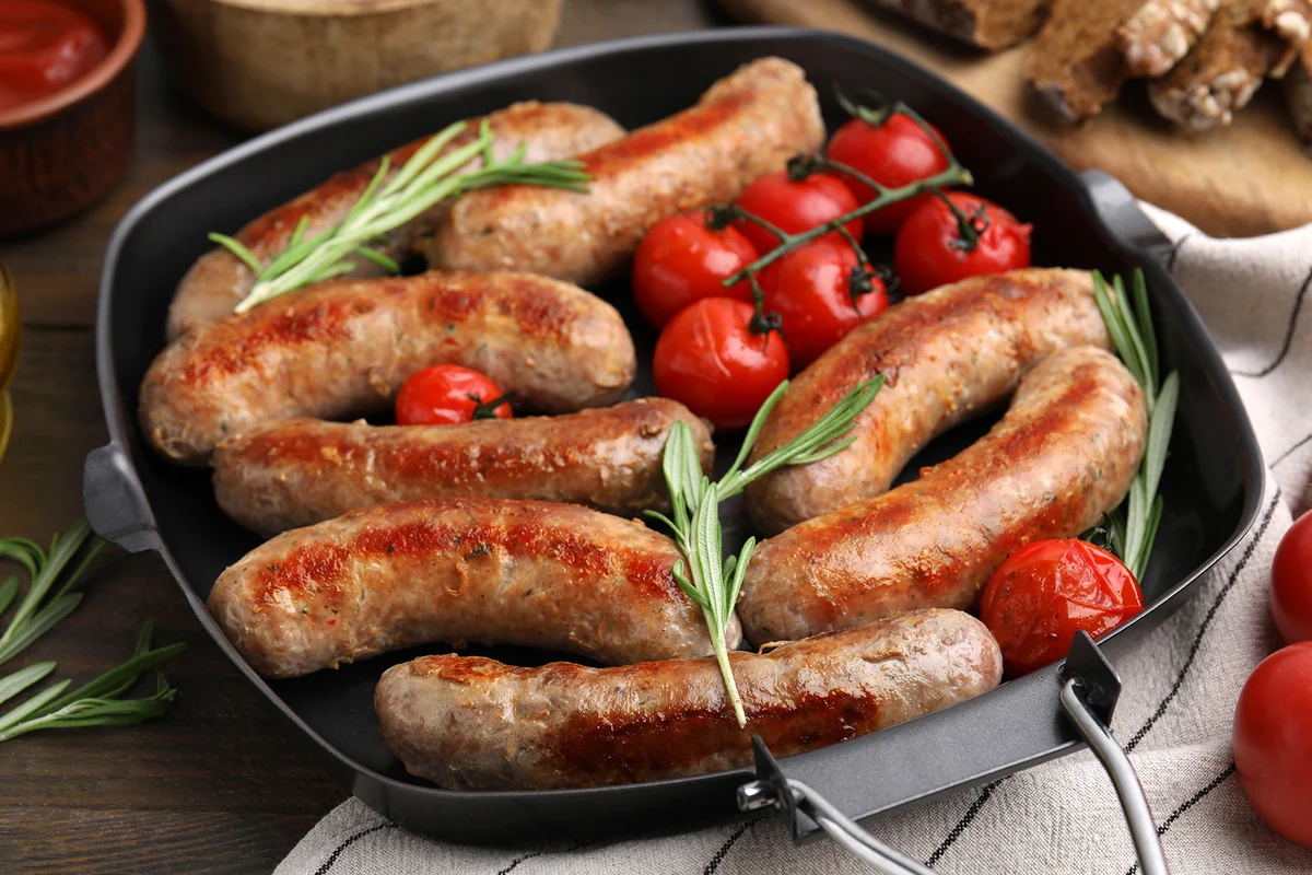 Grill pan with tasty homemade sausages, rosemary and tomatoes on wooden table