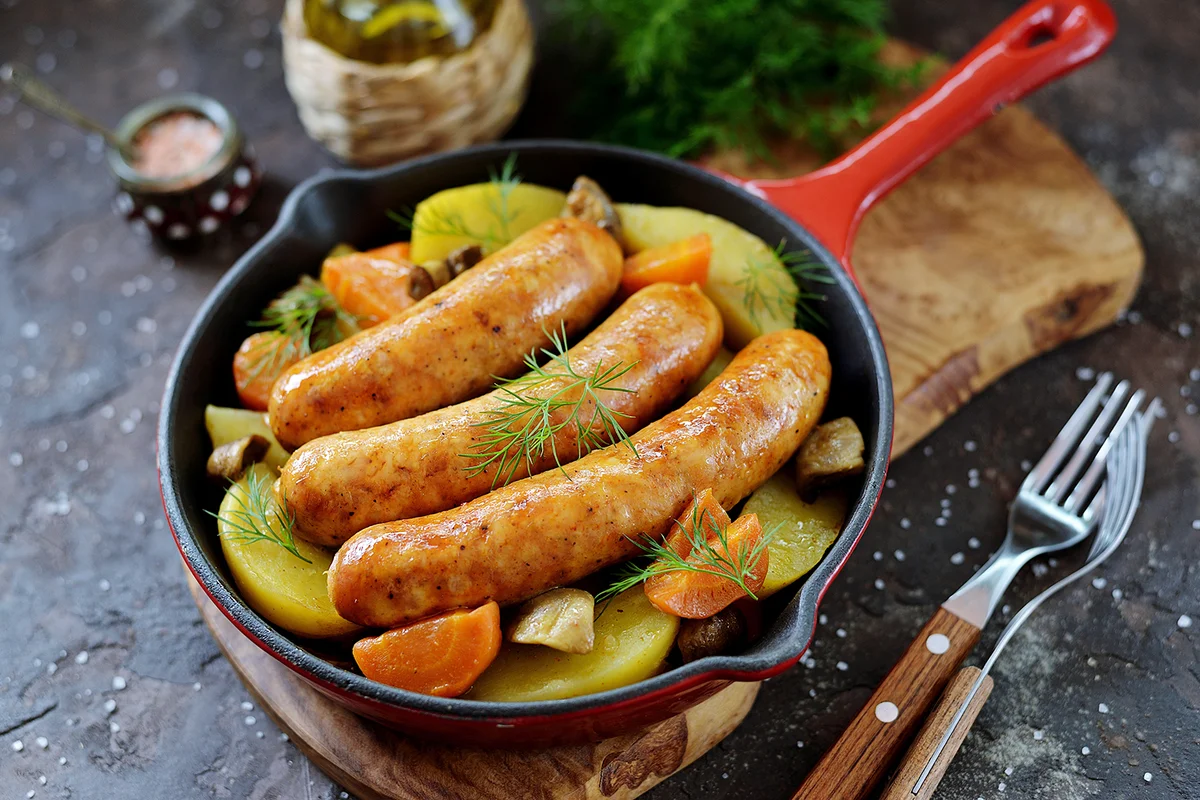 sausages with potatoes, onions, carrots and mushrooms in a cast-iron pan.