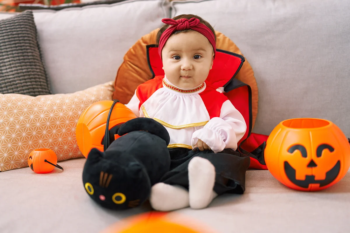 Adorable hispanic baby having halloween party holding pumpkin basket at home
