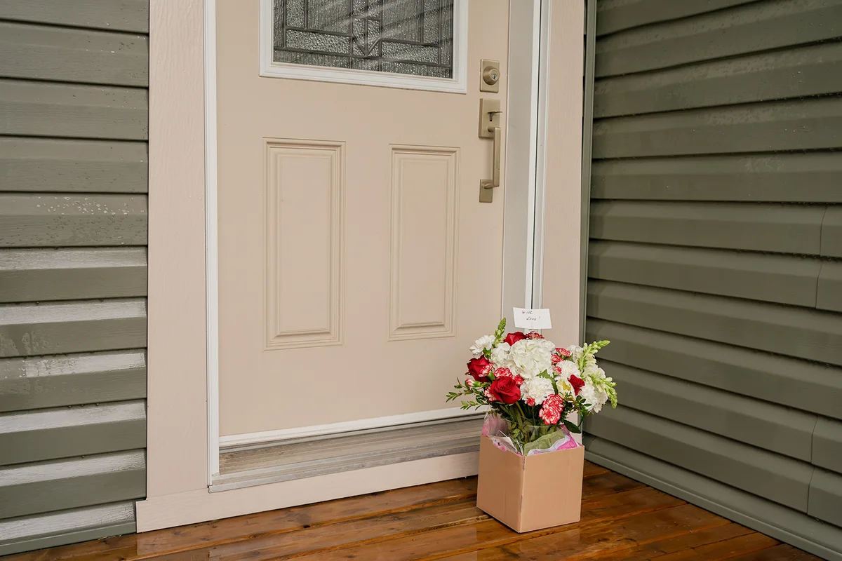 A bouquet of red white flowers in a carton box on a porch doorstep of a house