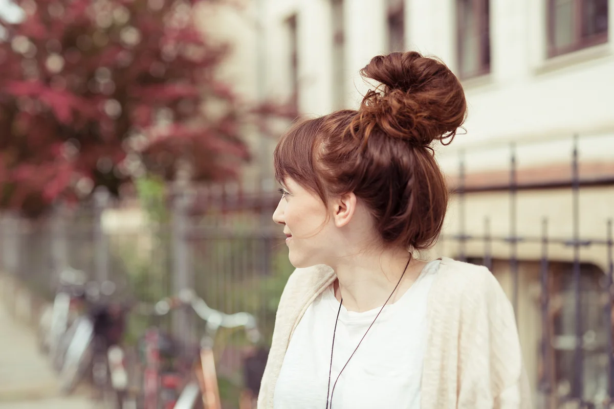 Attractive redhead woman with a fun hairstyle with her long hair wound into a high bun or top knot standing in an urban street,