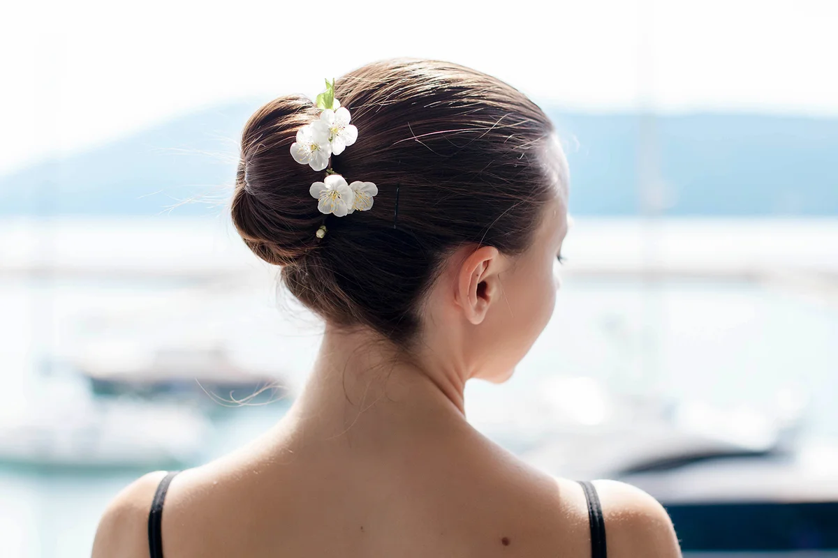Ballerina stands back and has hair bun with spring flowers.