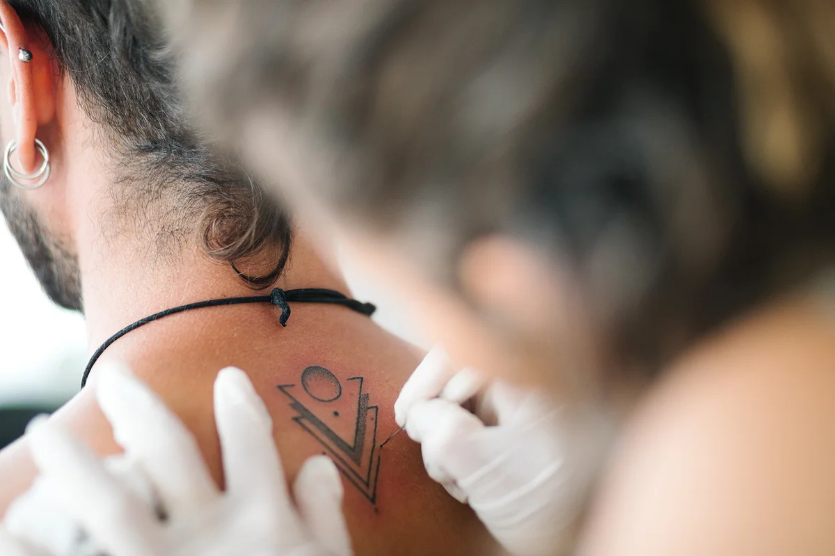 woman tattoing with Handpoke tattoo technique the back of a young man