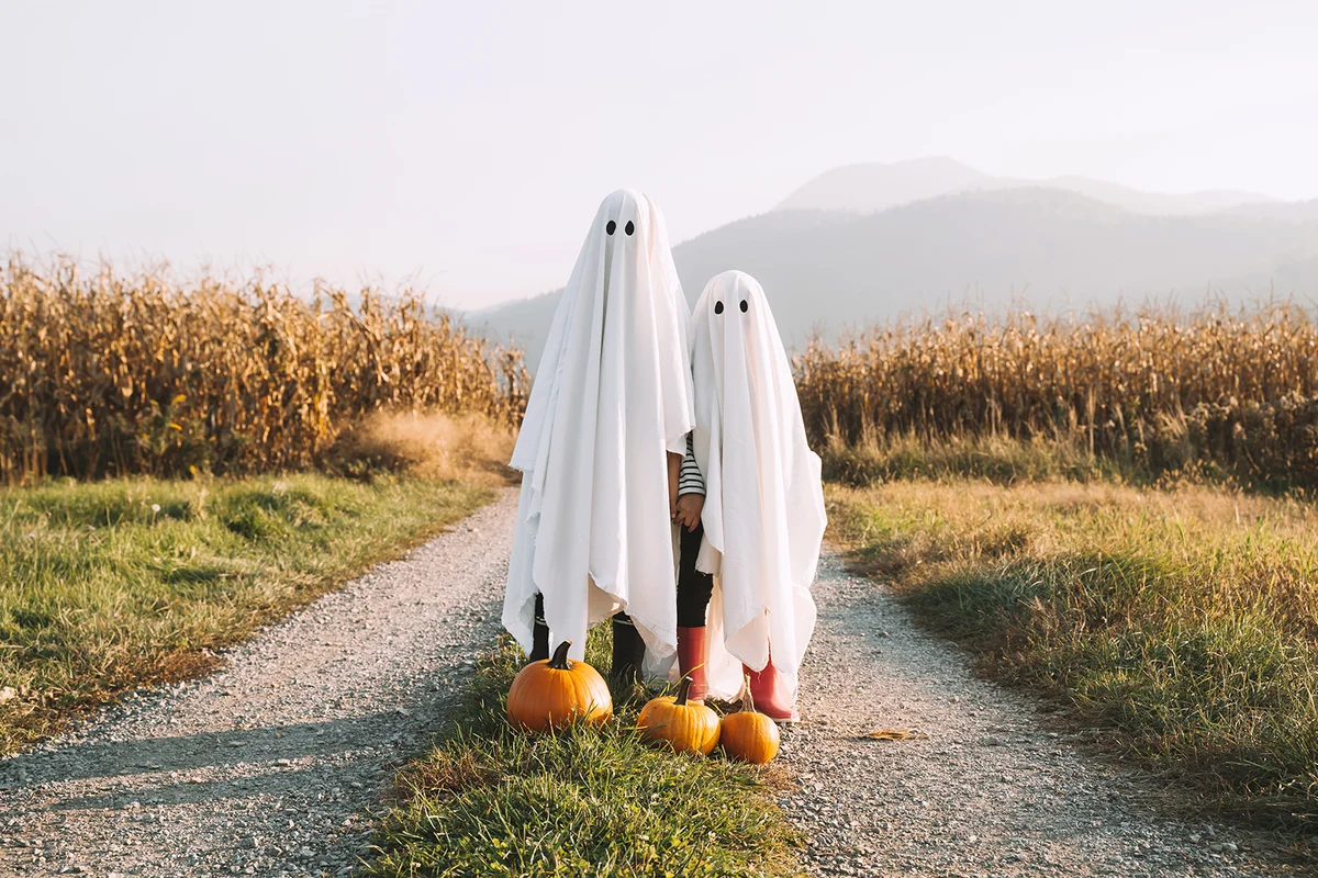 children dressed in white sheets like as cute ghosts