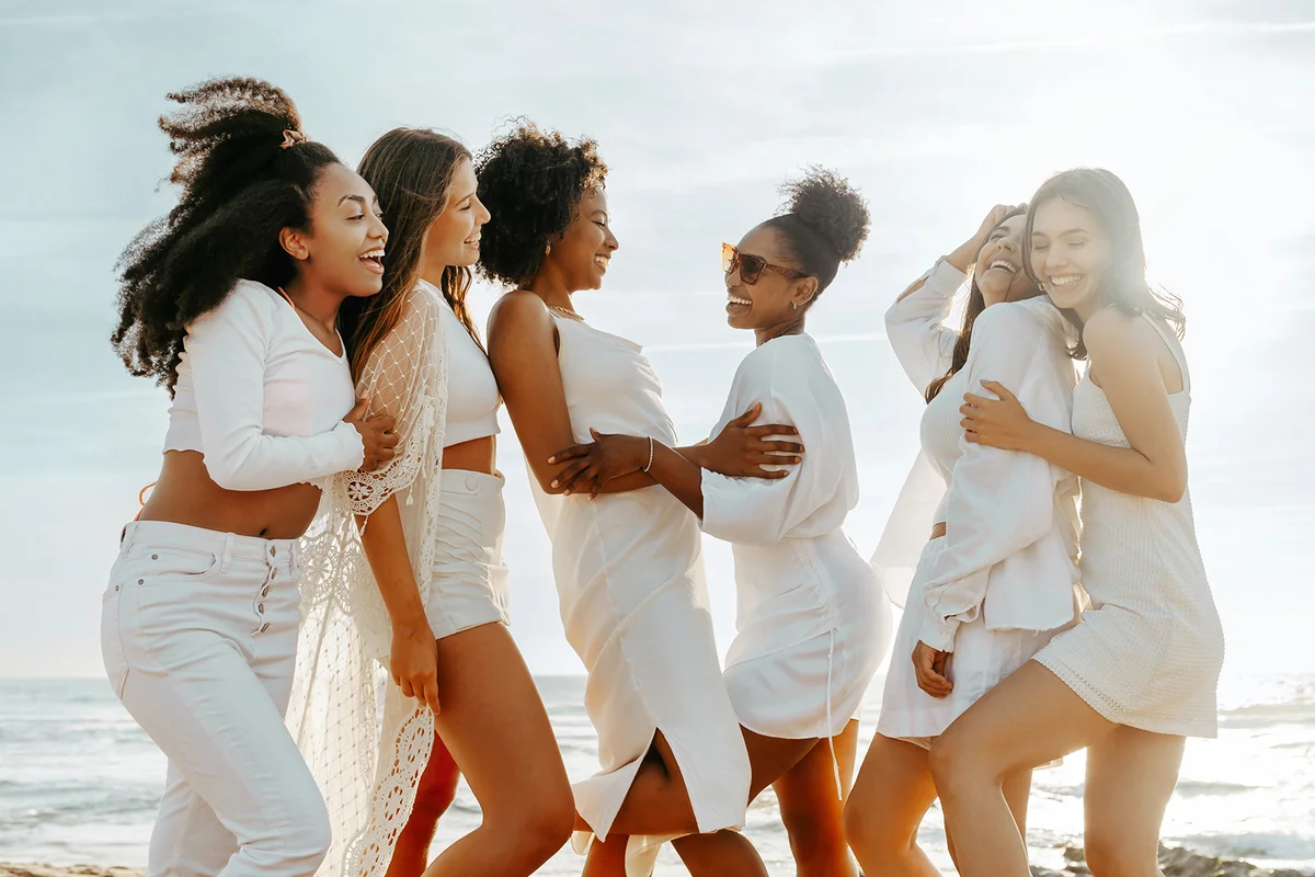 Happy diverse women posing on the beach, having fun and laughing, enjoying hen party celebration outdoors on ocean shore.