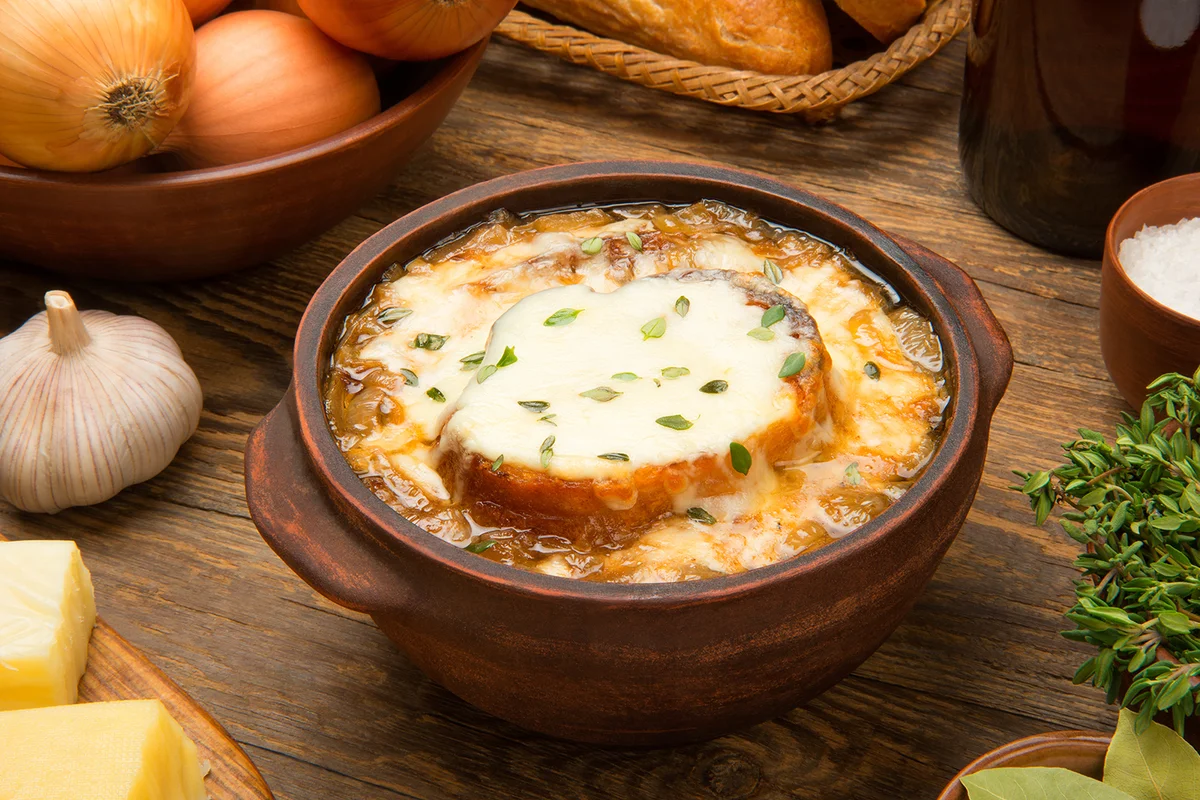 French onion soup in a brown ceramic bowl on a rustic wooden table