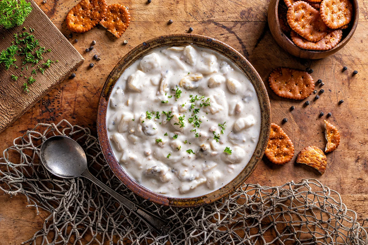 A bowl of delicious homemade New England clam chowder with parsley garnish and salted crackers