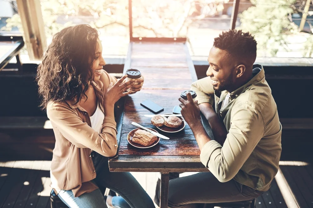 Two multiracial friends have coffee and pastries in a cozy café