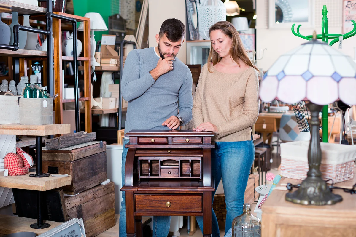 Young thoughtful couple choosing vintage writing cabinet in store of antique furniture