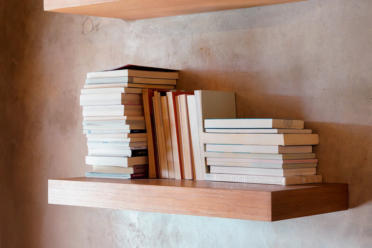 Stack of books on floating wooden bookshelf.