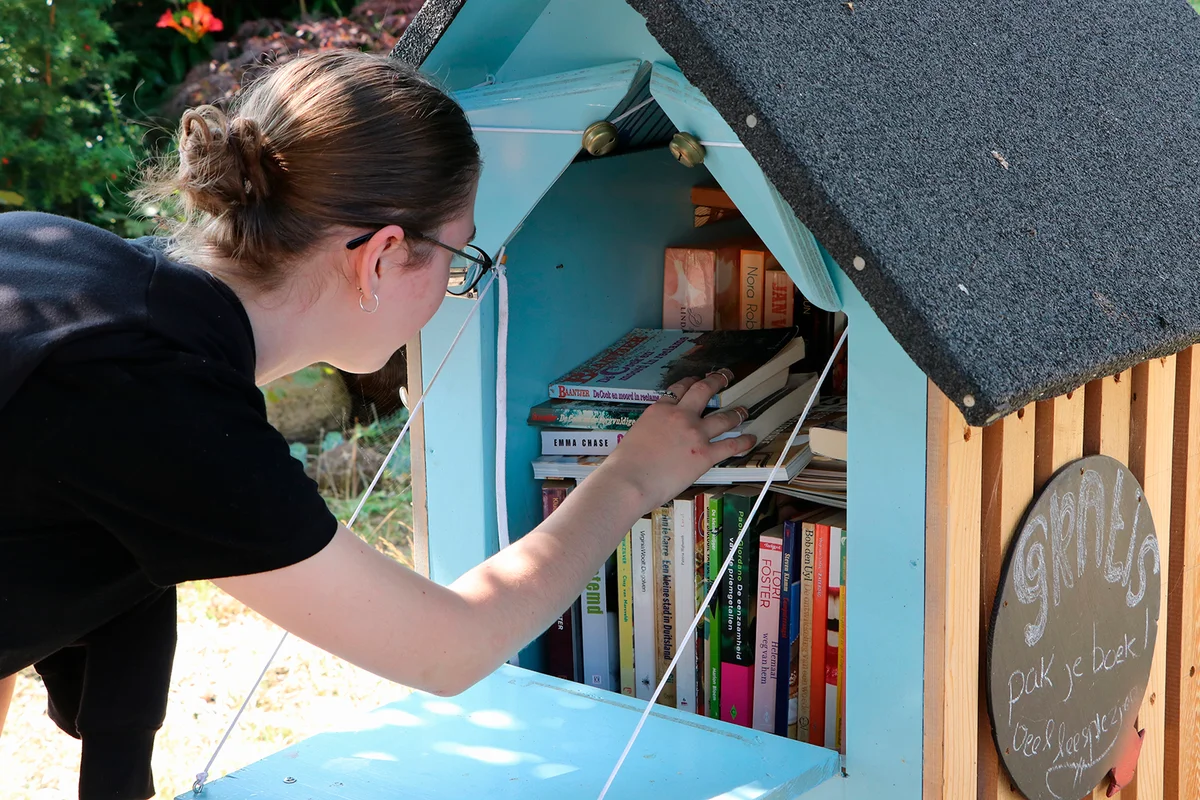 Teenage girl picking book from free library on street