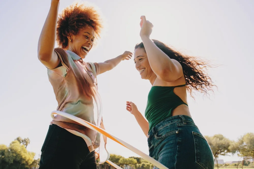 Two friends cheerfully playing with a hula hoop in the park.