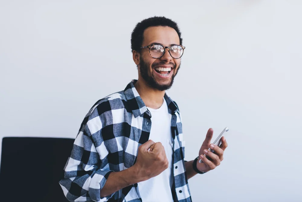 Joyful young man wearing glasses, making a success gesture with his hand.