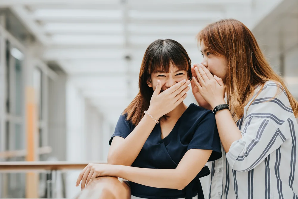 Young Asian girl whispering gossip or secret to her friend with a smile