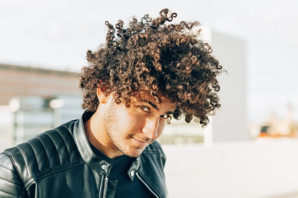 Outdoors portrait of a young man with curly hair and a sympathetic look