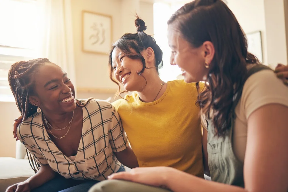 Three happy girlfriends speak and laugh while together on the couch