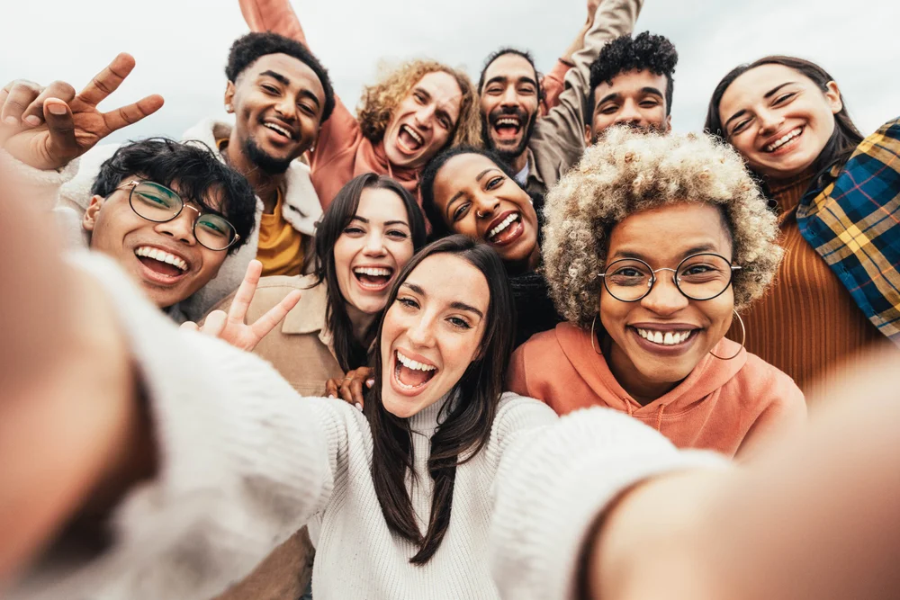A Leo woman takes a selfie with a big group of friends while laughing at the camera