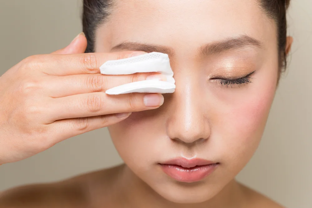 A young woman is removing eye makeup with cotton.