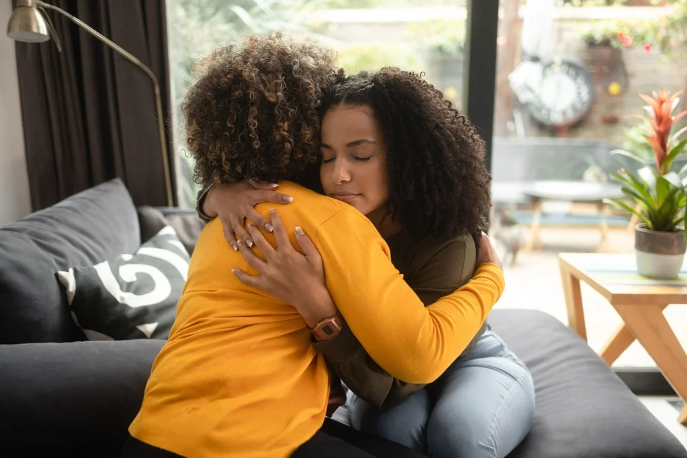 An African-American female comforts her friend hugging her.