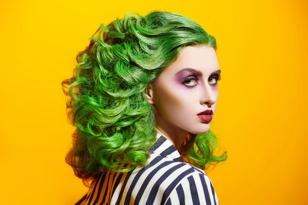 Close-up shot of a model with makeup and hair in the style of Beetlejuice on a yellow background