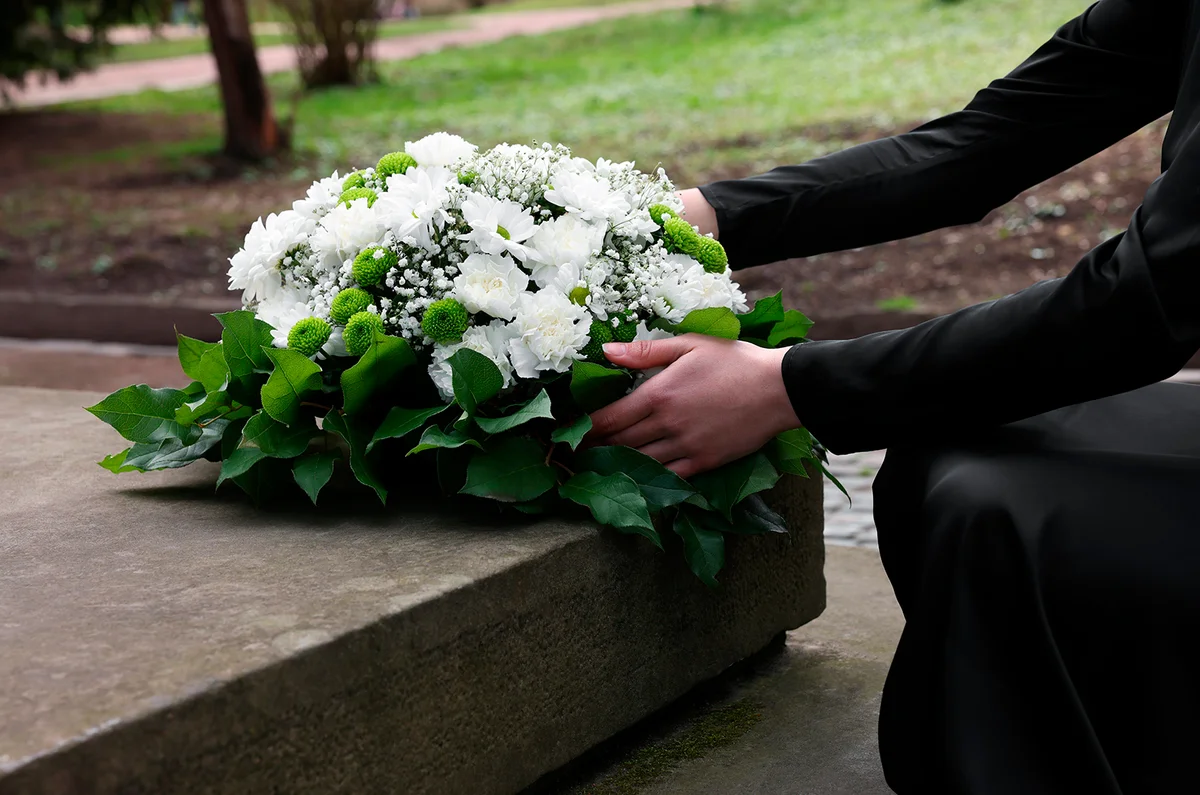 Woman with wreath of flowers near tombstone outdoors