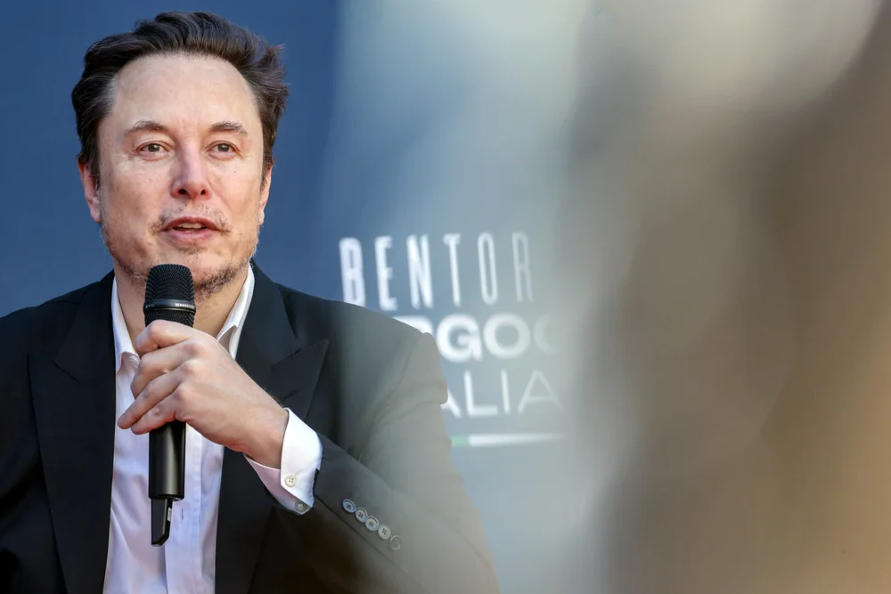 Portrait of Elon Musk holding the microphone at a conference.