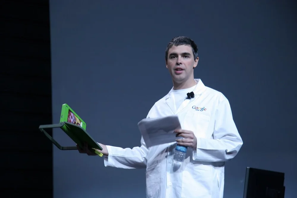 Larry Page at a conference with wearing a white Google uniform