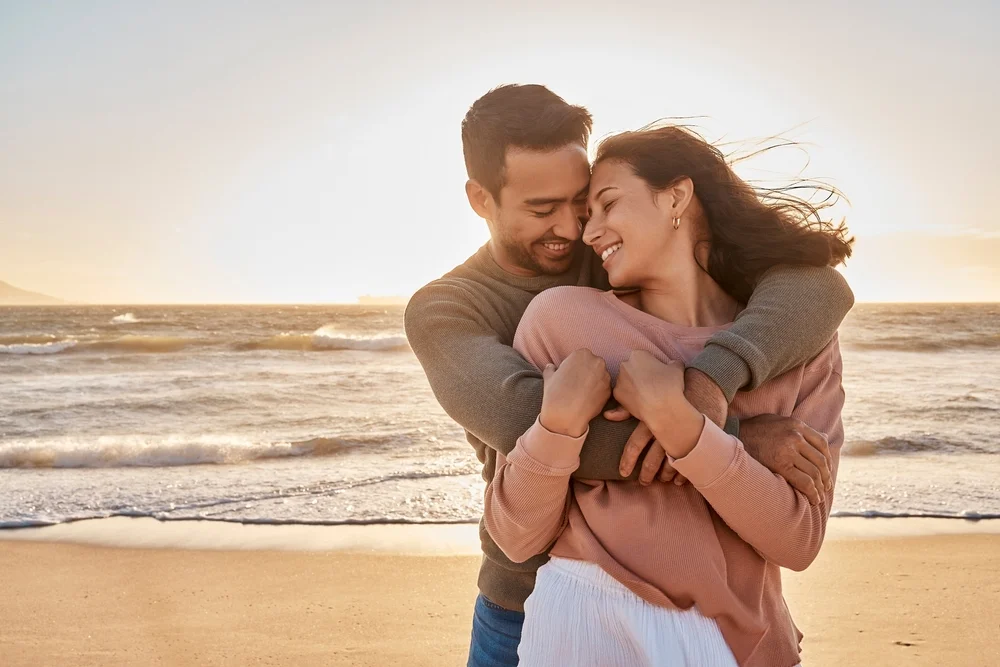Young diverse couple joyfully hugging at the beach together during sunset