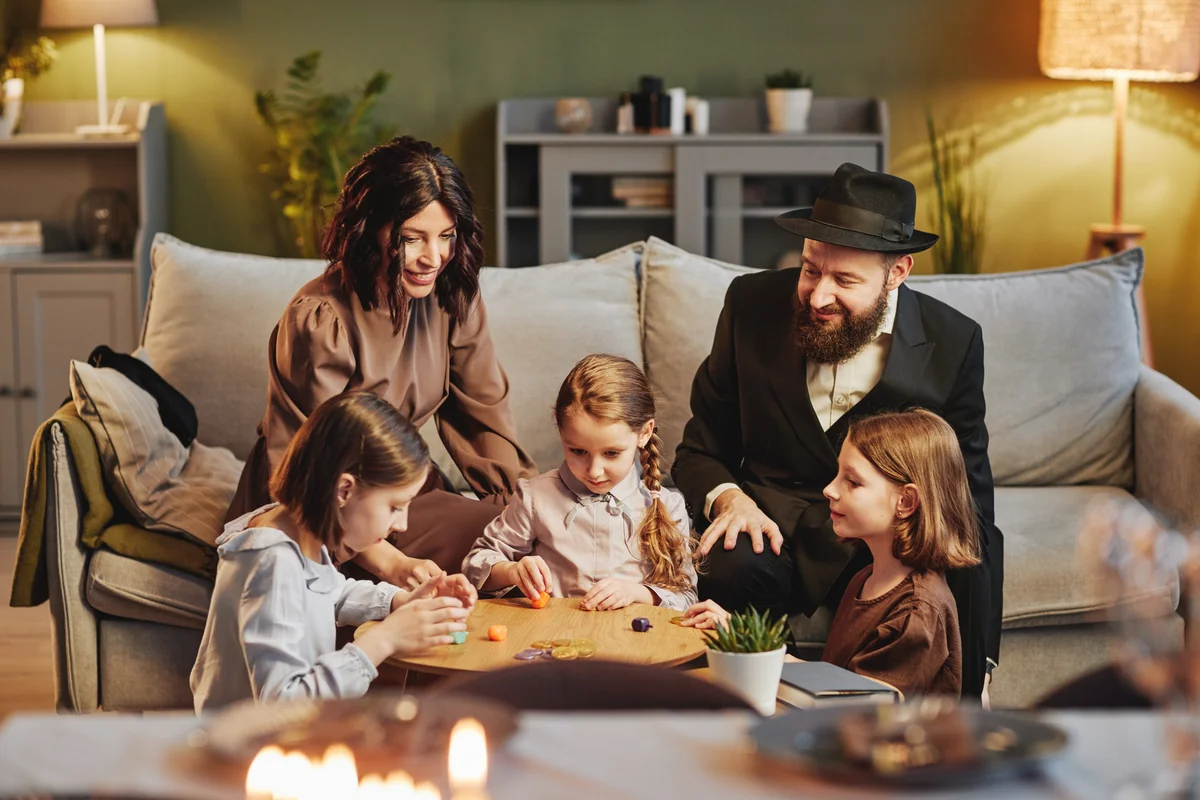 A modern Jewish family sits together in their living room spinning dreidels.