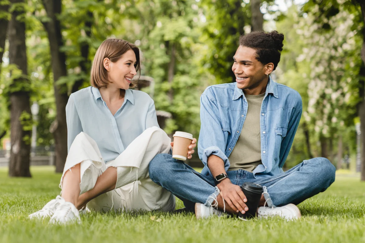 Young couple sits on the grass in a park talking to each other.