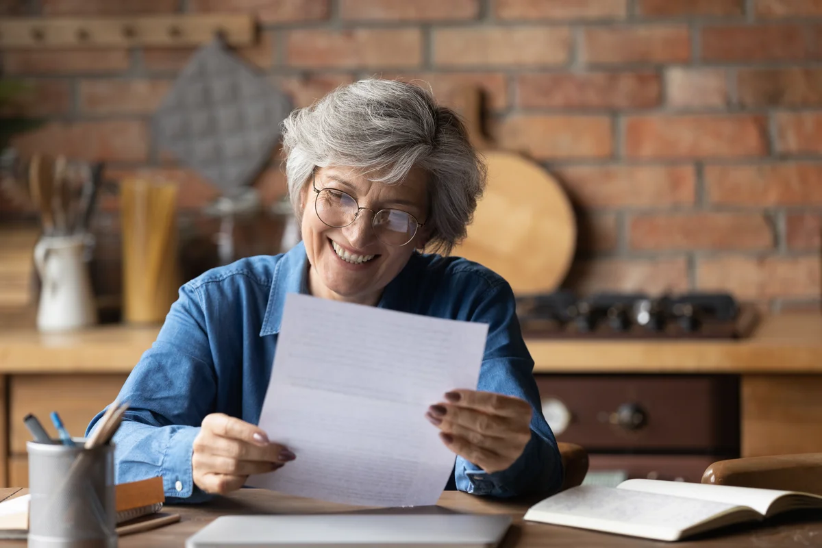 A woman sits at a desk and looks at a piece of paper in her hands.