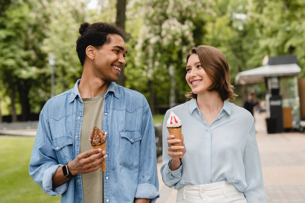 A couple looks at each other while holding ice cream in their hands.